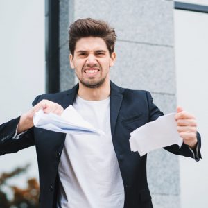 Serious businessman tearing contract in pieces. Angry furious male office worker throwing crumpled paper, having nervous breakdown at work, screaming in anger, stress management